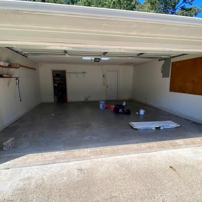 An empty, well-lit residential garage with beige walls, a concrete floor, and an open doorway leading to a back room.