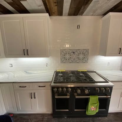 A kitchen with white cabinets, a subway tile backsplash, a patterned accent tile above a black gas stove, and wood ceiling.