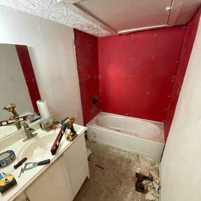 A bathroom under renovation with red waterproof backer board installed around a white bathtub and tools on the vanity.