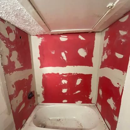 Bathtub area under renovation with red waterproof membrane applied over drywall seams and fastener spots.