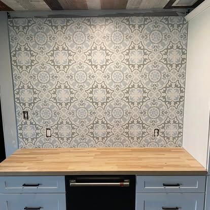 A kitchen backsplash with light blue and white patterned tiles above a light wood countertop and blue cabinets.