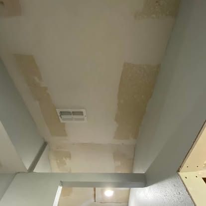 A ceiling with unfinished patches of light-colored spackle or drywall compound between sections of gray-painted wall.