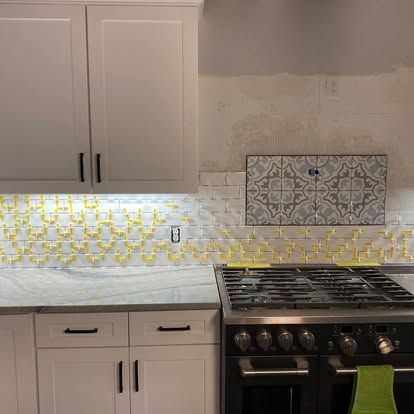 A kitchen featuring white cabinets, a light stone countertop, and a partially tiled backsplash with yellow spacers.