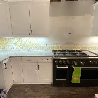 White kitchen cabinets installed above a dark wood floor with a black gas range and yellow honeycomb-patterned backsplash.