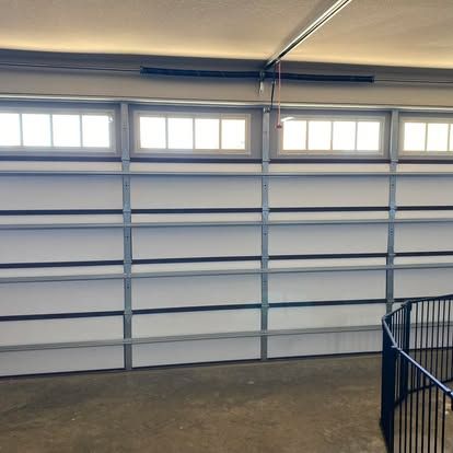 A white horizontal paneled garage door with rectangular windows along the top row, seen from inside a garage.