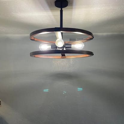 A modern, two-tiered circular chandelier with a black frame and three glowing filament light bulbs.
