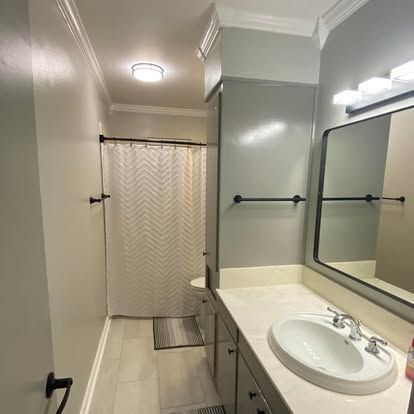 A bright, neutrally colored bathroom featuring a single-sink vanity, a large wall mirror, and a chevron shower curtain.
