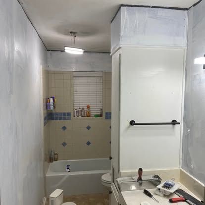 A bathroom under renovation with exposed drywall, a white vanity, a bathtub, and tiled walls with blue diamond accents.