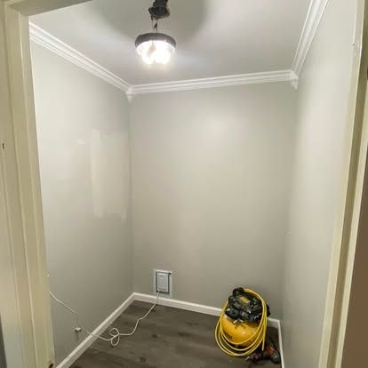 A small, empty closet with light gray walls, white trim, a ceiling light, and a yellow air compressor on the floor.