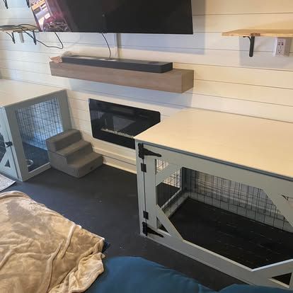 Two light-gray custom dog crates flank a fireplace and wall-mounted TV in a room with white shiplap walls.