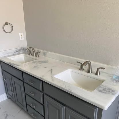 Double vanity with a white marble countertop, grey cabinets, and two undermount sinks with brushed nickel faucets.