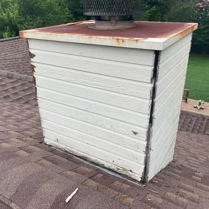 A weathered chimney chase cover with rusted top flashing and a vertical crack down the side on a shingled roof.