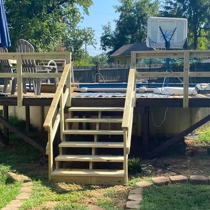 Wooden deck steps leading up to an above-ground pool area with chairs and a basketball hoop in a backyard setting.