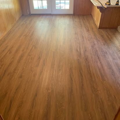 A newly installed wood-look laminate floor in an interior room with light wood paneled walls and a door in the background.