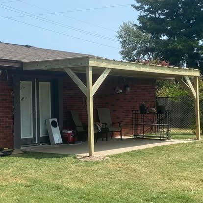 A newly constructed wooden patio cover attached to the back of a red brick house with a concrete slab patio.