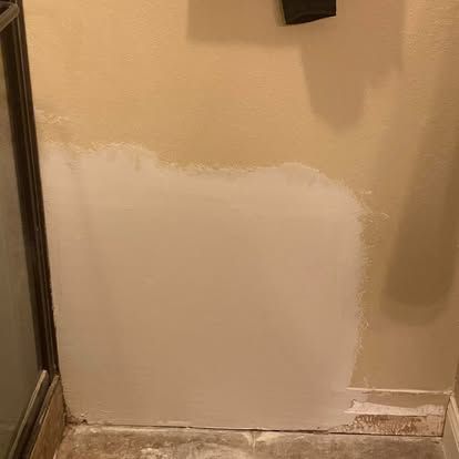A beige interior wall with a patch of fresh white drywall compound applied to the lower half.