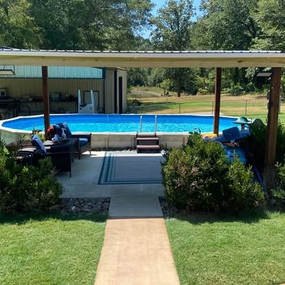 A backyard scene featuring an oval above-ground swimming pool under a wooden pergola, with a patio area and lawn.