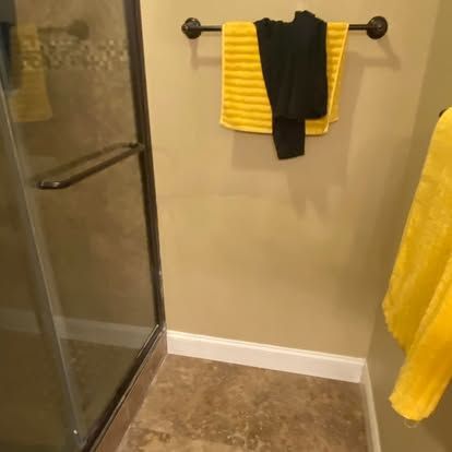 A bathroom interior showing a glass shower door next to a wall with a towel rack holding a yellow towel and black item.