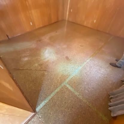 A room with wood-paneled walls and a worn, mottled brown floor featuring prominent intersecting seam lines.