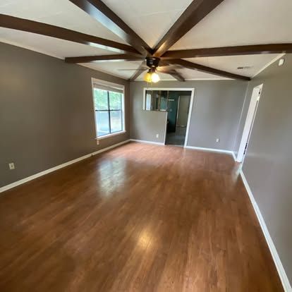 A spacious room with dark brown walls, wooden floors, and a vaulted ceiling with exposed decorative wood beams.