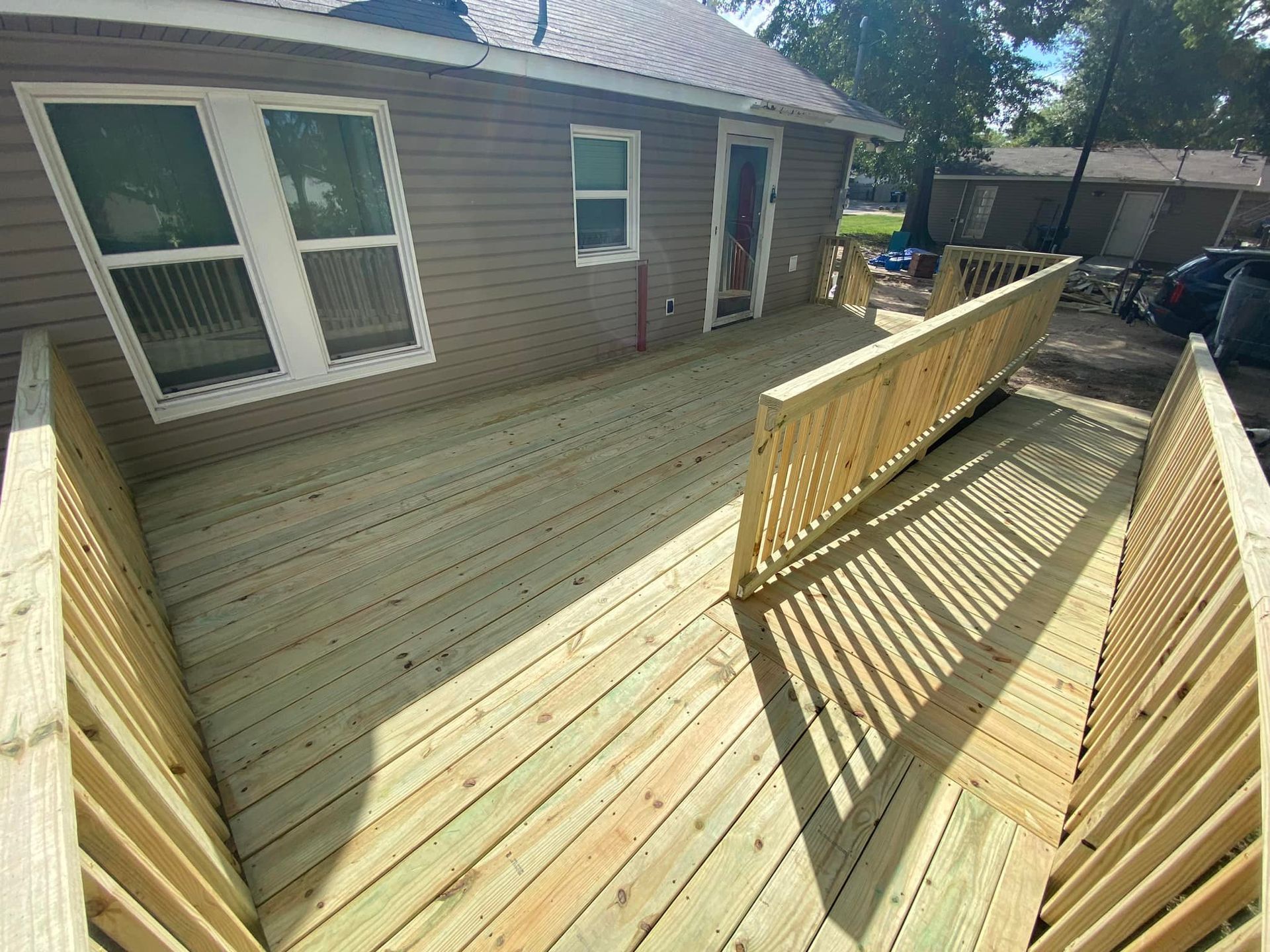 A newly constructed wooden deck featuring a ramp and safety railings attached to the side of a house with grey siding.