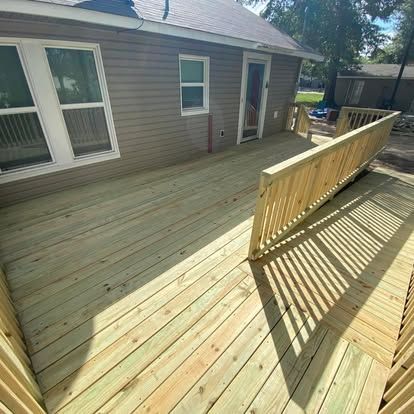 A newly constructed wooden deck featuring light-colored planks, a railing, and a ramp attached to a brown-sided house.