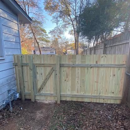A new, light-colored wooden fence and gate installed in a backyard next to the side of a light blue house.