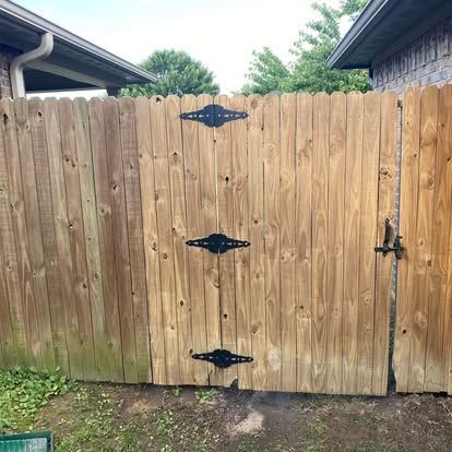 A wooden fence with a gate, featuring three black decorative hinges and a black latch, set between two building eaves.