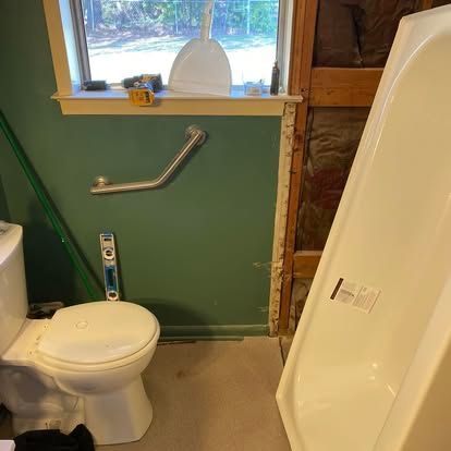 Bathroom in progress with a white toilet, grab bar on a green wall, window with a dustpan, and a new white bathtub.