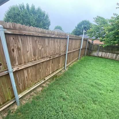 A wooden privacy fence with metal support posts borders a grassy lawn under a cloudy sky.