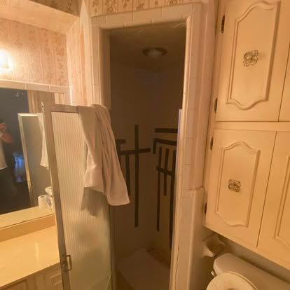 A bathroom featuring a shower stall with black tape geometric designs on the interior walls, next to a vanity and toilet.