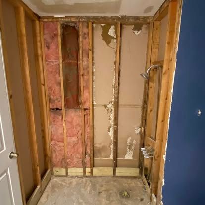 A partially demolished bathroom shower area with exposed wooden wall studs, insulation, and plumbing fixtures.