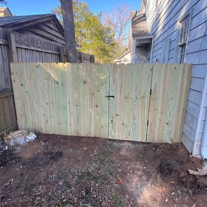 A newly installed light-colored wood fence and gate section between a house and an older wooden fence in a yard.