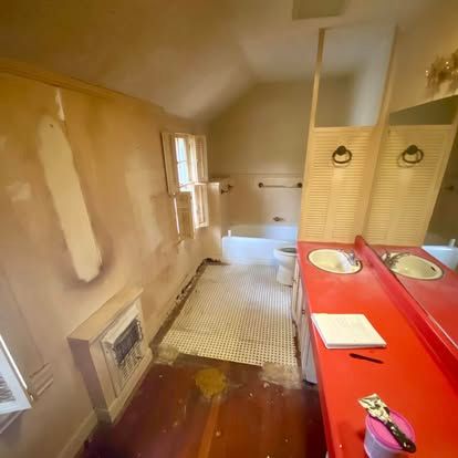 A bathroom undergoing renovation features a bright red vanity, checkered tiled floor, and a white bathtub.