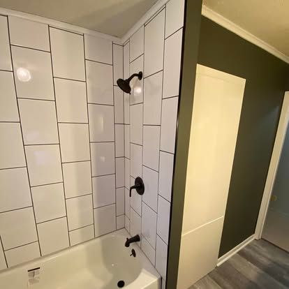 A white subway-tiled shower with matte black fixtures and a dark green accent wall in a modern bathroom.