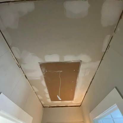 A ceiling repair showing a new drywall patch and joint compound applied over the seams in a hallway.