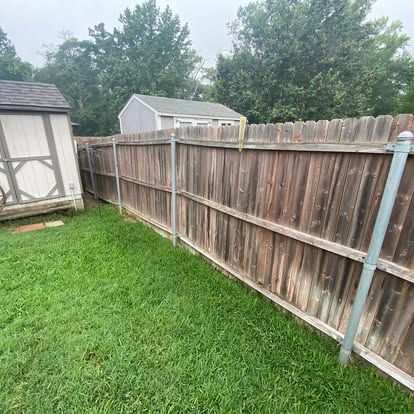 A wooden privacy fence with metal support posts in a backyard with a shed and green grass.