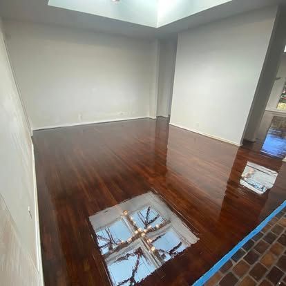 An empty room with polished, dark-brown hardwood floors reflecting a large skylight and white walls.