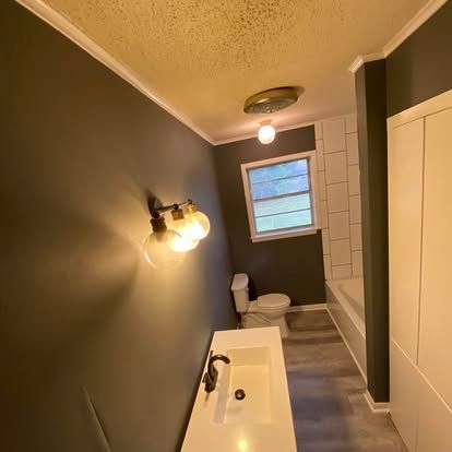 A modern bathroom with dark green walls, a white vanity with a dark faucet, a toilet, and a light-colored wood floor.