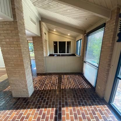 A sunroom features a reddish-brown brick floor, a white brick pillar, a half-wall, and windows with white blinds.