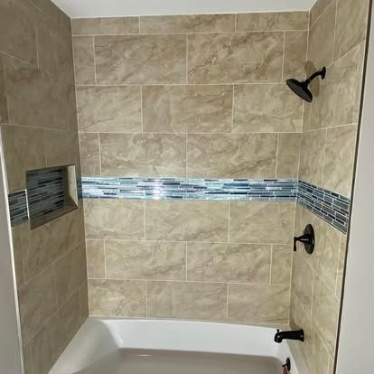 A bathtub shower with beige marble-look tiles, a blue glass mosaic accent strip, and black shower fixtures.