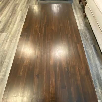 A rectangular, dark brown wood-grain table surface seen from a high angle, set on light wood-look floor planks.