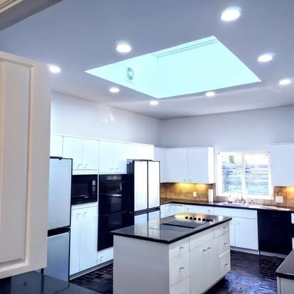 A modern kitchen with white cabinets, dark countertops, a central island, stainless steel appliances, and a skylight.