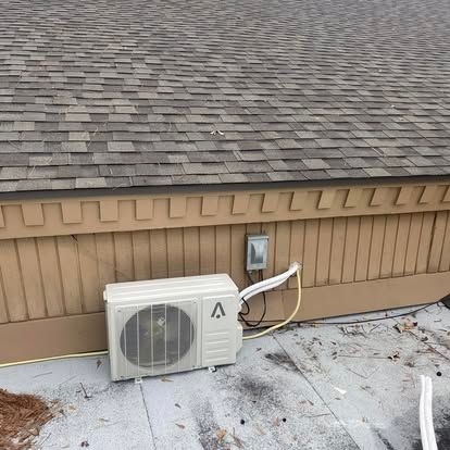 An outdoor mini-split AC unit sits on a flat, gray roof against a beige, wood-paneled wall with visible wiring.