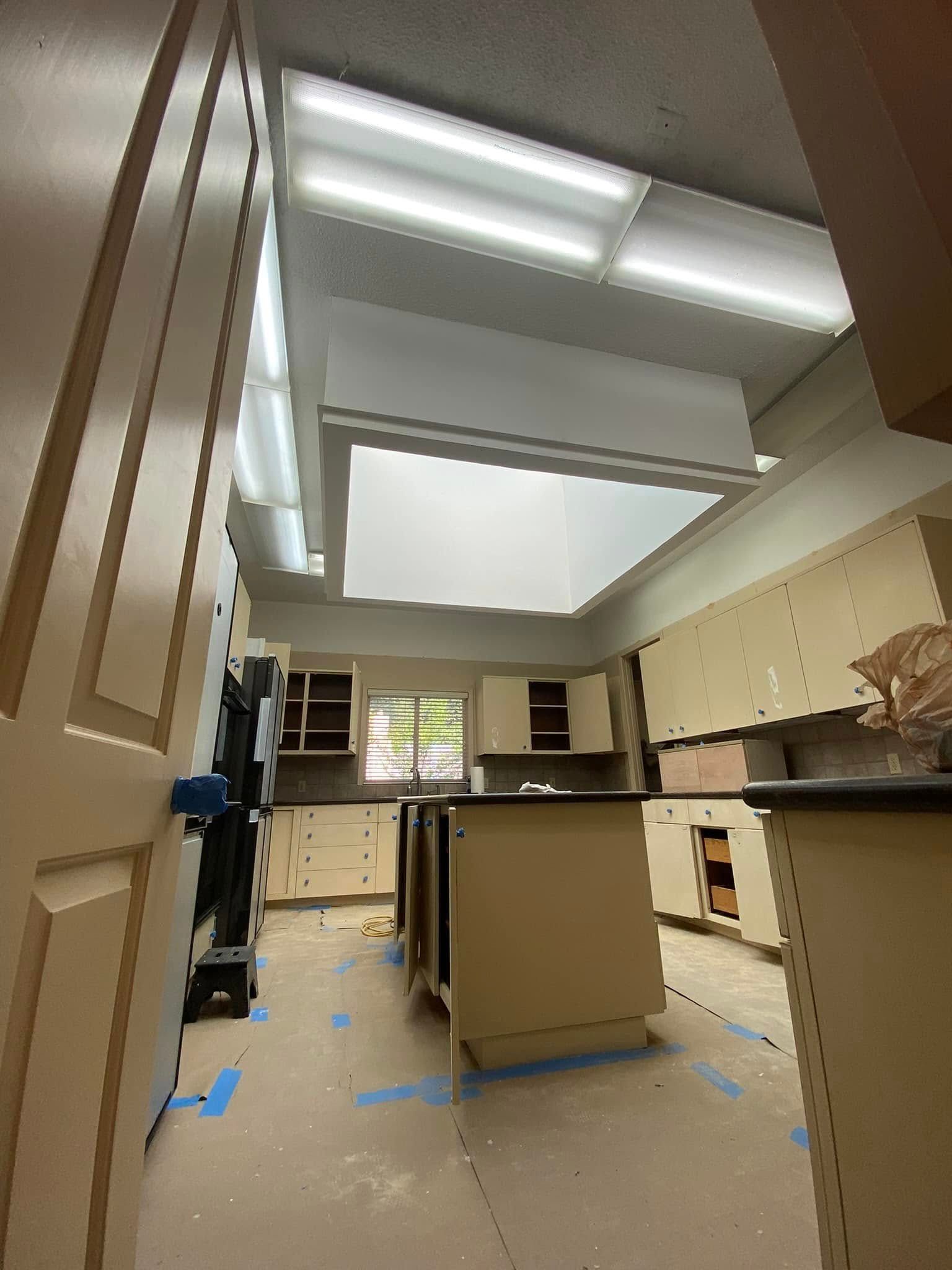 A kitchen interior under renovation with light-colored cabinets, a central island, and a skylight in the ceiling.