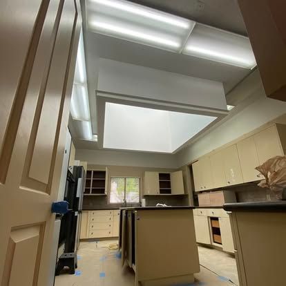 A renovated kitchen with light-colored cabinets, a central island, recessed lighting, and a large skylight.