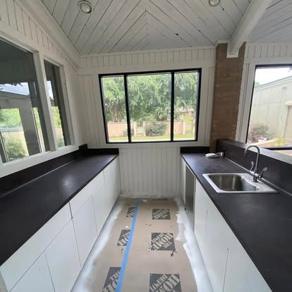 A modern galley-style kitchen with white cabinets, dark countertops, a sink, and floor protection paper under construction.