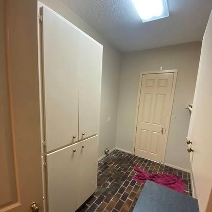 A room with a tall, white cabinet on the left, a brick floor, and a white door in the back.