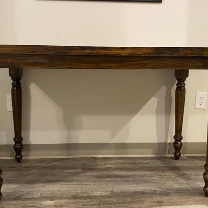 A dark wood console table with turned legs stands against a white wall with an electrical outlet.