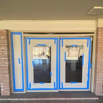 Double doors and a side panel with blue painter's tape and protective plastic masking, set within a brick frame.
